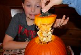 seeds coming out of carved pumpkin with kid looking on in background