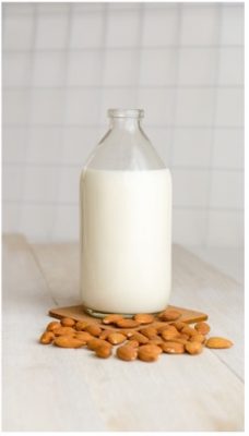 glass bottle of almond milk and almonds scattered loose on counter